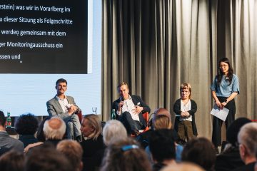 2 Personen sitzen auf der Bühne, 2 Personen stehen daheben.